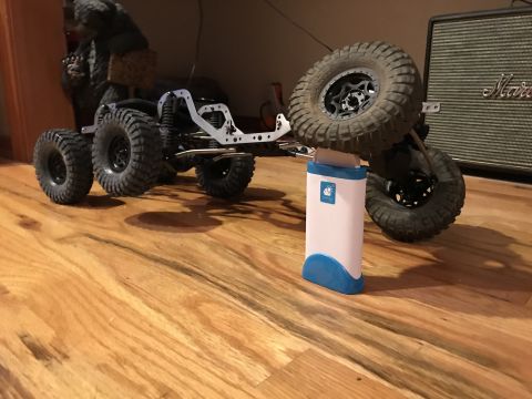 1989 Ford Bronco - RC crawler chassis with six wheels and a spare tire, sitting on a wooden floor.