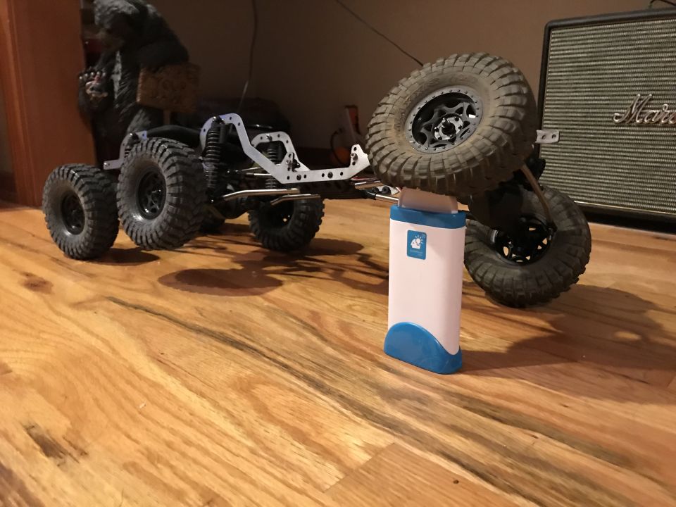 RC crawler chassis with six wheels, spare tire mounted, and a blue/white object underneath