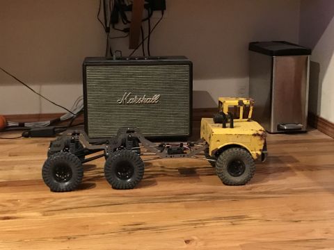 1989 Ford Bronco - A custom RC rock crawler with a yellow body and exposed chassis sits on a wooden floor.