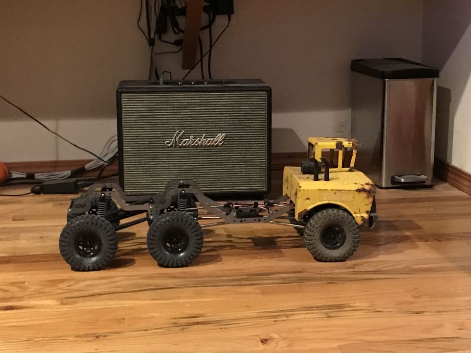 RC rock crawler chassis with a yellow body and six wheels, next to a Marshall amplifier