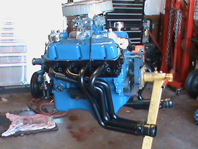 Blue engine with black headers on a yellow engine stand, with an air filter on top