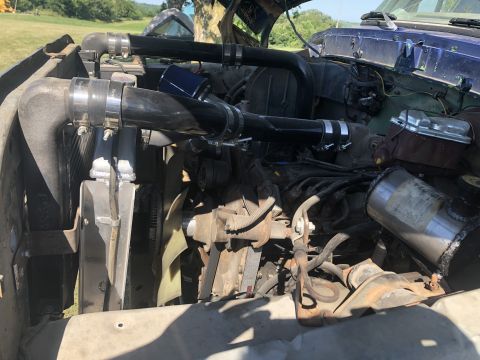 1979 Ford Bronco - The engine bay of a vehicle is shown with modifications to the intake system.