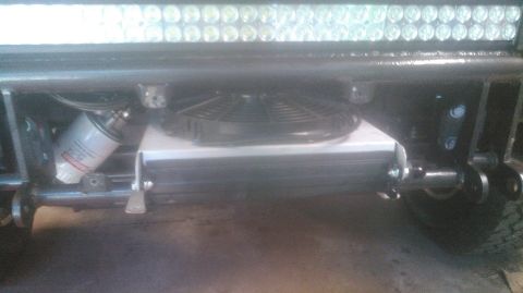 1992 Ford Bronco - A close-up view shows a black electric fan mounted on top of a silver oil cooler, with a white oil filter to the left, all installed beneat…