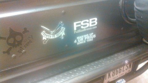 1992 Ford Bronco - A close-up view of the rear driver's side of a dark-colored vehicle, likely an SUV, showing several stickers and a license plate.