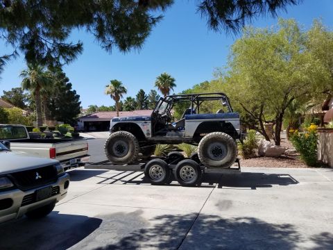 1979 Ford Bronco - A modified Ford Bronco, likely a 1979 model based on context, is loaded onto a trailer. The vehicle features a roll cage, large off-road ti…