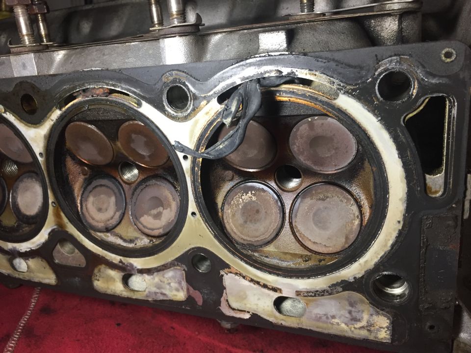 Disassembled engine cylinder head with valves and gasket.