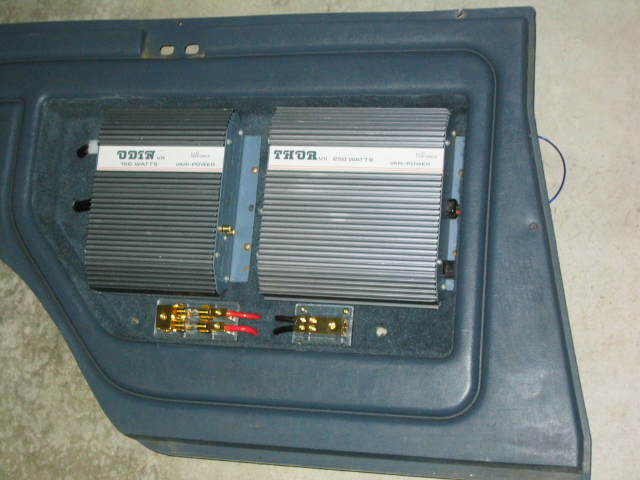 Two car amplifiers labeled Odin and Thor mounted on a blue carpeted vehicle panel
