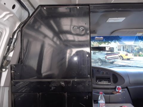 1999 Ford E250 - Interior view of a van, showing a black metal partition behind the driver's seat. Outside the van, a white pickup truck and a yellow car ar…