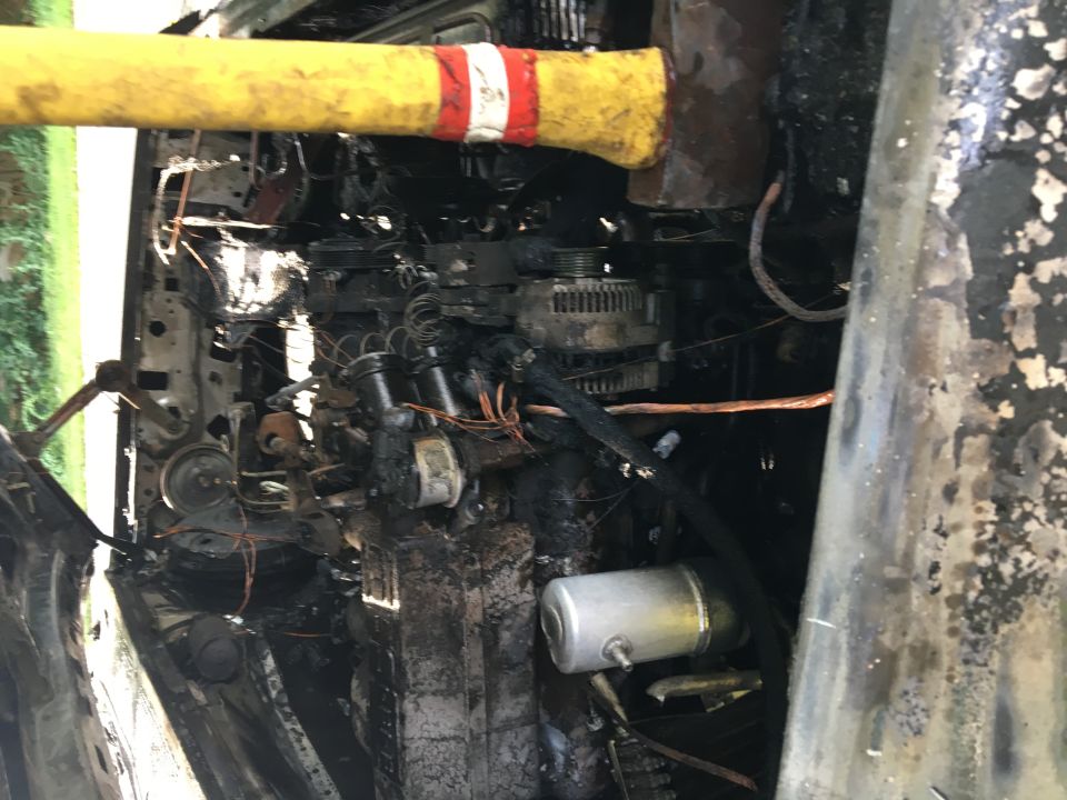 Burned engine bay with a yellow and red striped tool over it.