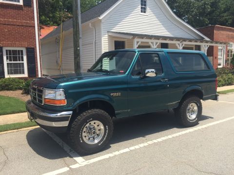 1996 Ford Bronco - A green 1996 Ford Bronco is parked on a street in front of a building.