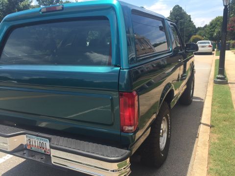 1996 Ford Bronco - The rear of a teal Ford Bronco is shown parked on the side of a street with a white car in the background.