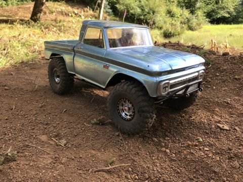 1989 Ford Bronco - A toy pickup truck with off-road tires sits on a dirt path surrounded by greenery.