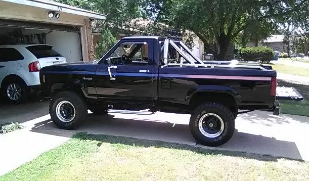 Black 1987 Ford Ranger pickup truck with a roll bar, parked in a driveway next to a white SUV