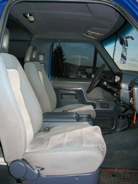 1989 Ford Bronco - The interior of a blue truck features cloth seats and a center console, with a view of the outdoors through the windows.