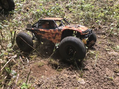 1989 Ford Bronco - A remote control rock crawler navigates a rough, wooded terrain with large, knobby tires.