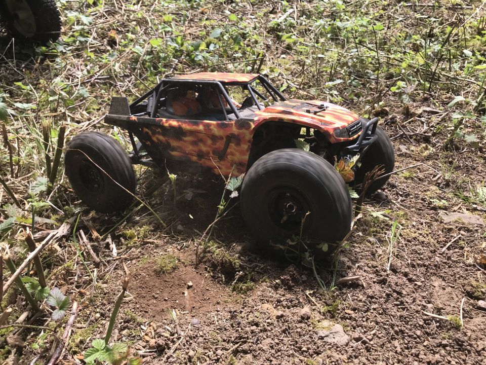 Orange and black camouflage remote control rock crawler with large tires on a dirt path