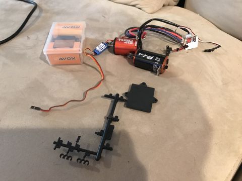 1989 Ford Bronco - Various electronic components and plastic parts for an RC car are laid out on a textured surface.