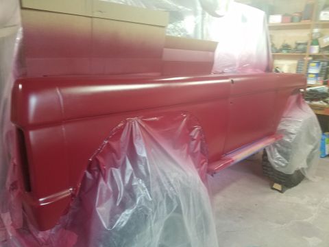 1968 Ford Bronco - Vehicle body, likely a 1968 Ford Bronco, is being prepped for paint with red primer and plastic sheeting.