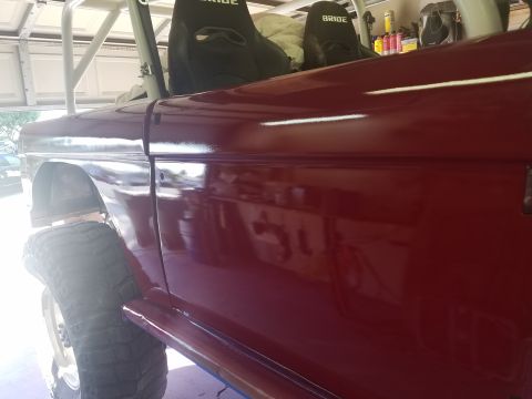 1968 Ford Bronco - A maroon Ford Bronco with racing seats and a roll cage is viewed from the side, with a visible tire and fender.