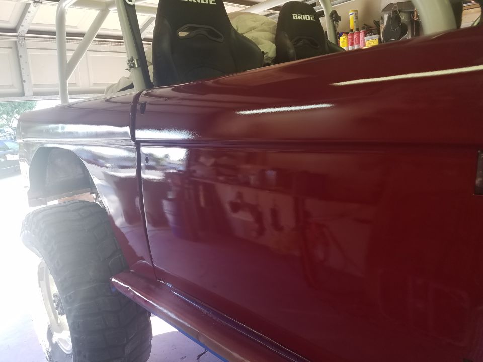 Maroon Ford Bronco side view, showing roll cage and Bride seats. Visible tire and fender