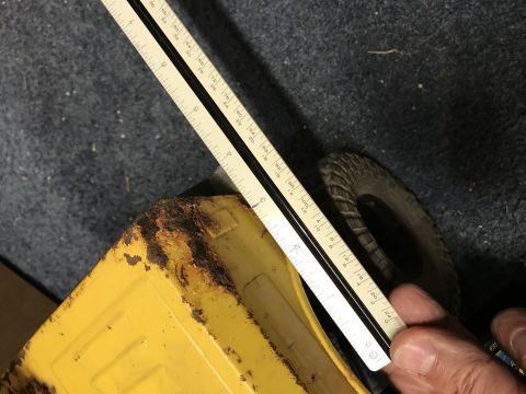1989 Ford Bronco - A ruler is placed over the rusted corner of a yellow toy truck bed, with a tire visible in the background.