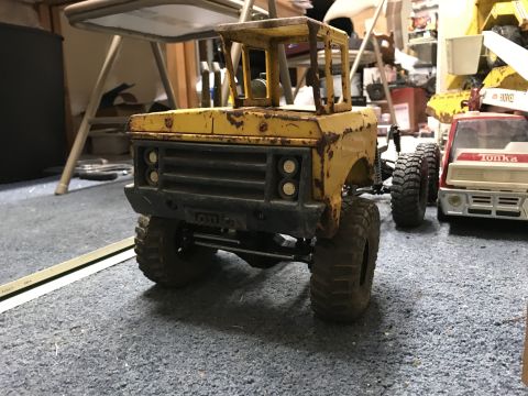 1989 Ford Bronco - A weathered yellow toy truck sits on a carpeted floor, with another toy vehicle visible to its right.