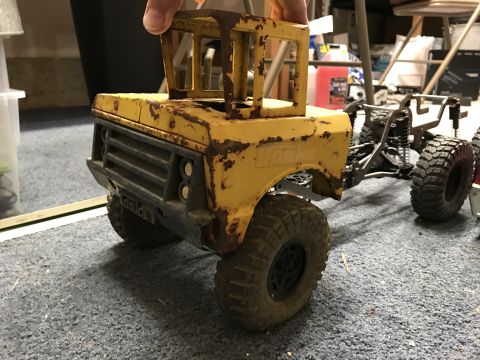 1989 Ford Bronco - A weathered yellow toy truck, possibly a Tonka, is held up, revealing its chassis and wheels.