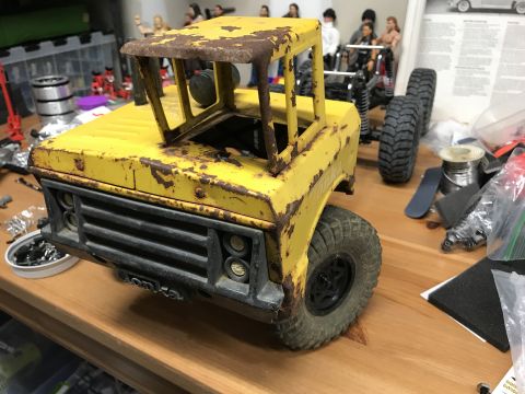 1989 Ford Bronco - A weathered yellow toy truck sits on a wooden surface, surrounded by various hobby parts and figures.