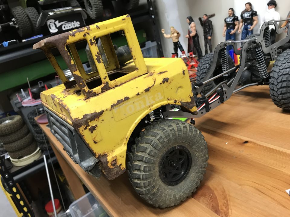 rusted yellow Tonka toy truck body on a metal chassis, with toy figures in background