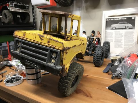 1989 Ford Bronco - A weathered yellow Tonka truck model sits on a stand, with other RC vehicles and a vintage advertisement visible.