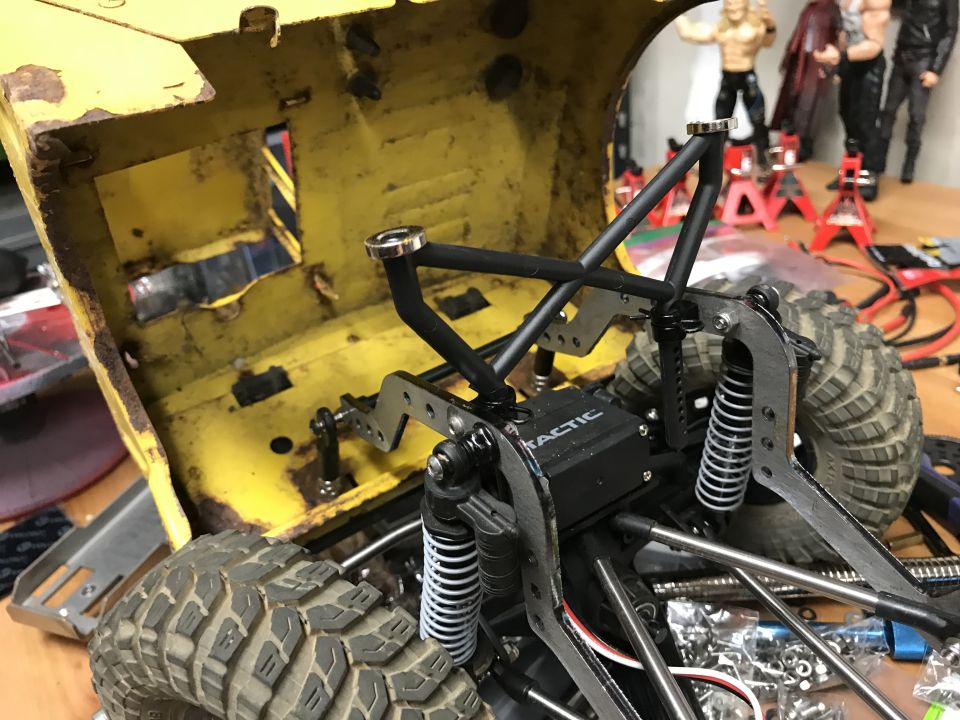 RC rock crawler chassis with yellow body shell, black roll cage, and large tires. Tactic electronics visible
