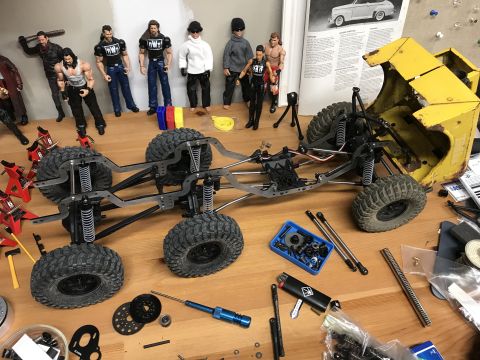 1989 Ford Bronco - RC crawler chassis and parts are assembled on a workbench, with action figures in the background.