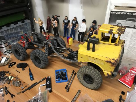 1989 Ford Bronco - A partially assembled toy truck sits on a workbench with various tools and action figures nearby.
