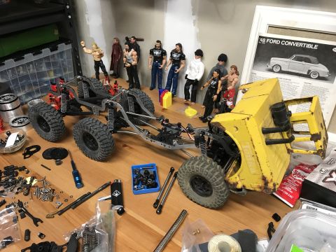1989 Ford Bronco - A yellow RC truck chassis sits on a workbench next to action figures and a poster of a 1948 Ford Convertible.