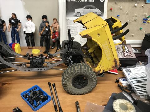 1989 Ford Bronco - RC car parts and figures laid out on a wooden workbench, ready for assembly.