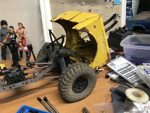 1989 Ford Bronco - A partially assembled yellow Tonka toy truck chassis sits on a workbench, surrounded by various parts and action figures.
