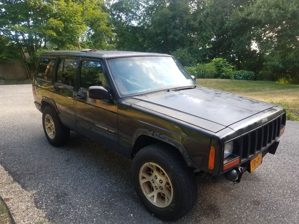 Black Jeep Cherokee XJ parked on asphalt, trees in background