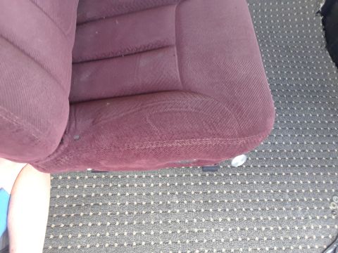 1999 Ford E250 - The interior of a vehicle shows a worn maroon seat next to a grey carpet with a white dot pattern.