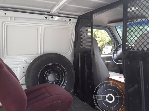 1999 Ford E250 - Interior view of a cargo van, showing a spare tire and a partition separating the cargo area from the driver's cabin.