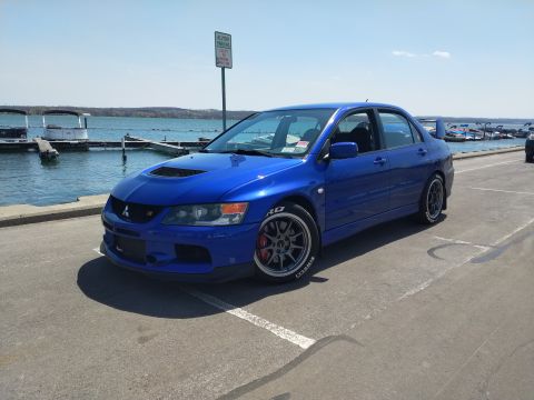 2006 Mitsubishi Evolution - A blue Mitsubishi Lancer Evolution VIII is parked near a body of water with boats docked.