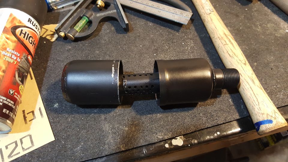 Black exhaust muffler part with perforated inner tube, next to a can of high-heat spray paint and a hammer handle