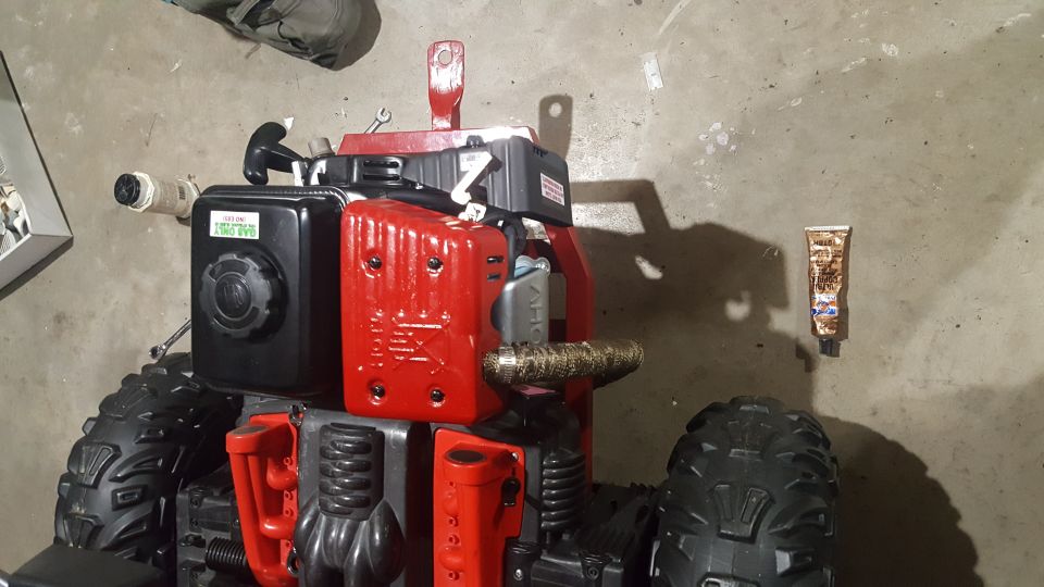 Red and black engine unit with large, knobby tires and a metal pull cord