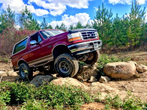 1995 Ford Bronco - This 1995 Ford Bronco is shown tackling a challenging off-road course with large rocks and uneven ground.