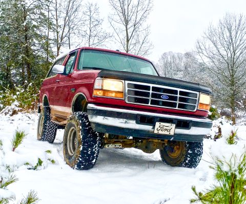 1995 Ford Bronco - A red Ford Bronco with a lifted suspension navigates through a snowy landscape.