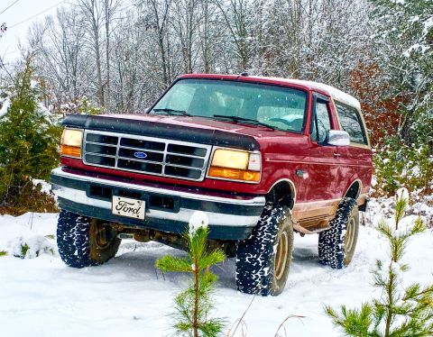 1995 Ford Bronco - Red 1995 Ford Bronco navigates a snowy, wooded area with its headlights on.
