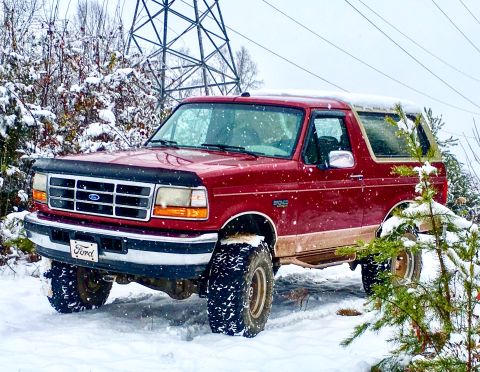 1995 Ford Bronco - A red Ford Bronco is parked in a snowy landscape with trees and a power line tower in the background.