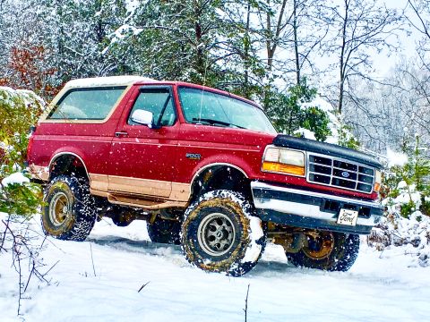 1995 Ford Bronco - Red 1995 Ford Bronco equipped for off-road conditions navigates a snowy landscape.
