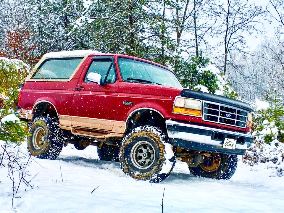 1995 Ford Bronco with lifted suspension driving in snow, front grille visible