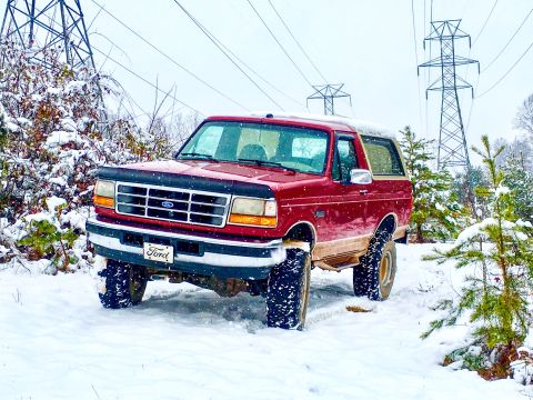 1995 Ford Bronco - This red Ford Bronco is parked in a snowy landscape with power line towers visible.
