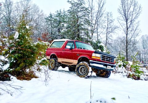 1995 Ford Bronco - A red Ford Bronco navigates a snow-covered forest road.